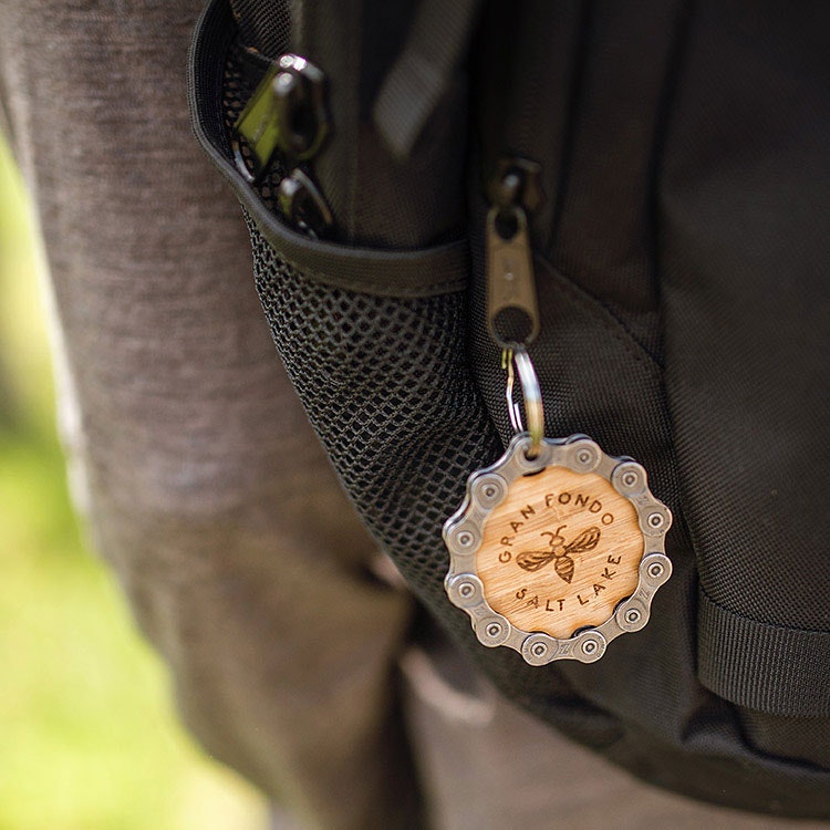 Round bamboo keychain clipped to a rider's backpack on the trail