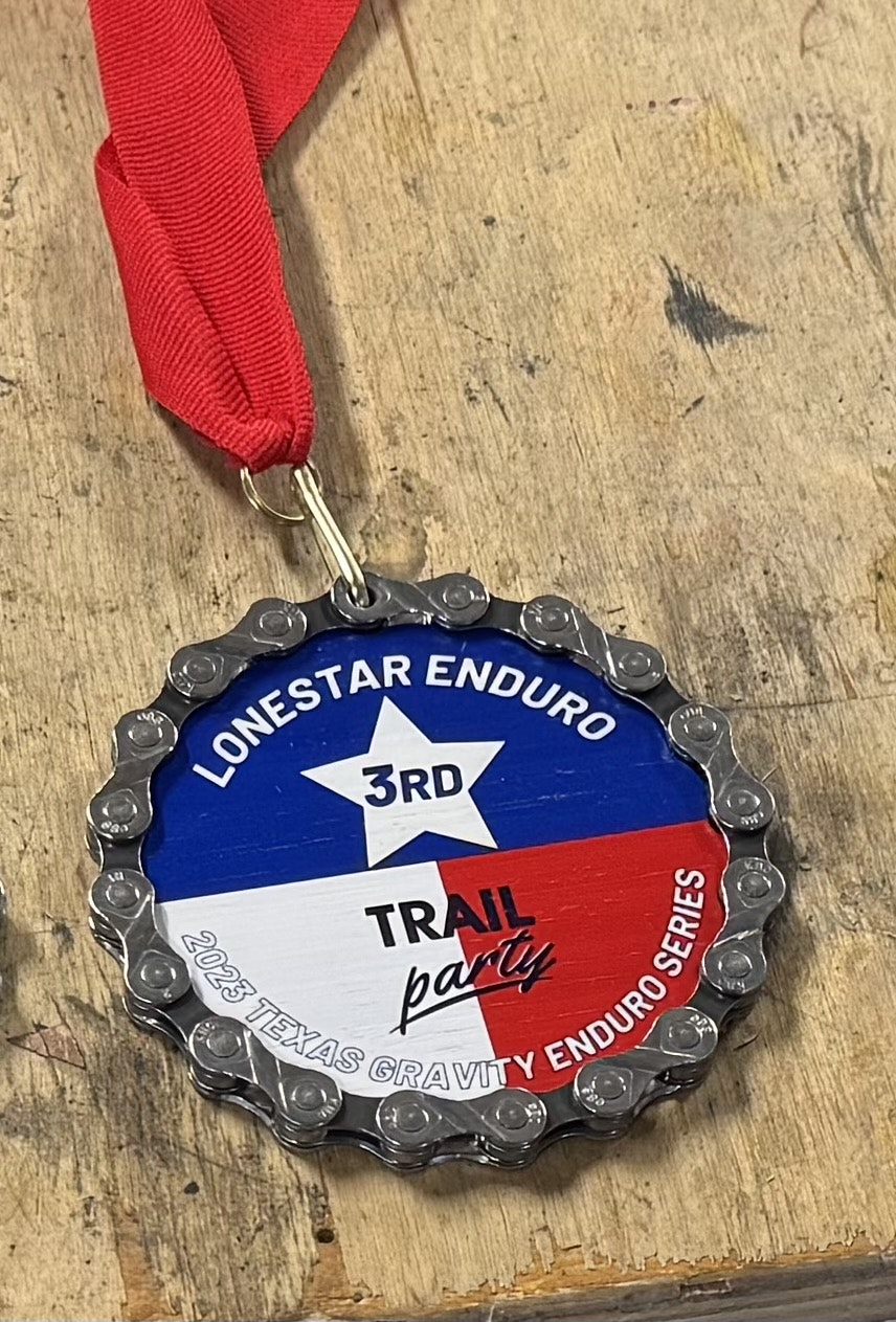 3-inch bamboo finisher medal with full-color print, wrapped in a reclaimed bike chain, on the workshop bench